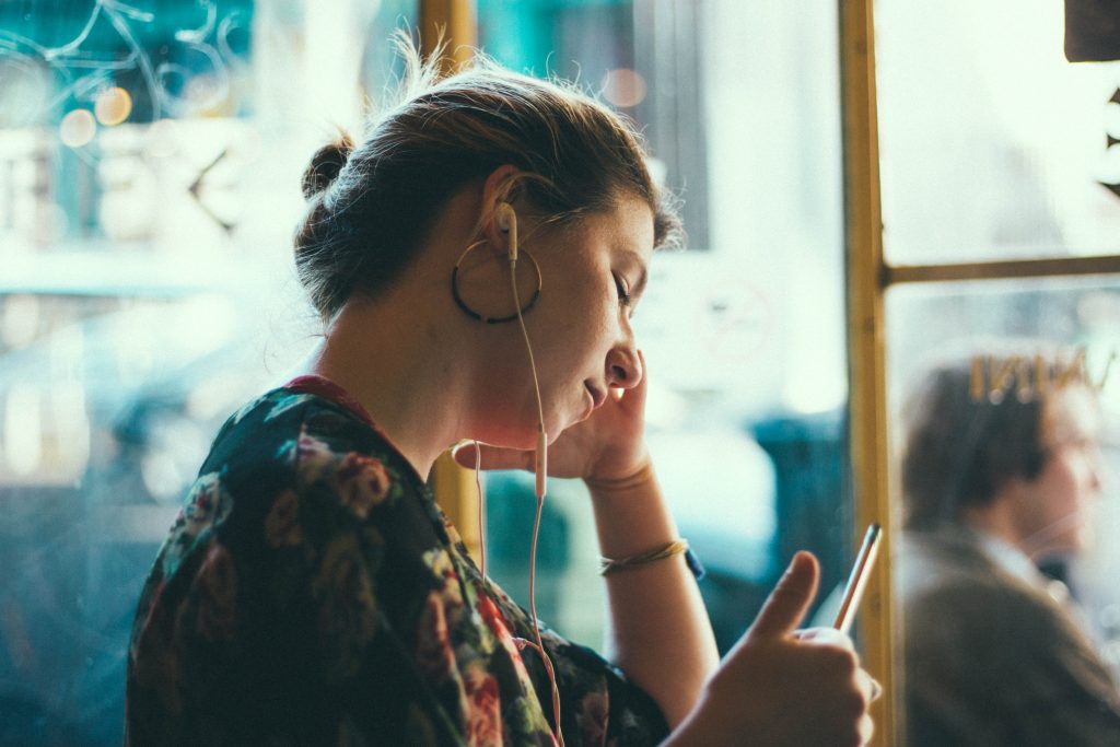 a lady wearing a ponytail hairstyle earphones in her ears, holding a looking at her phone